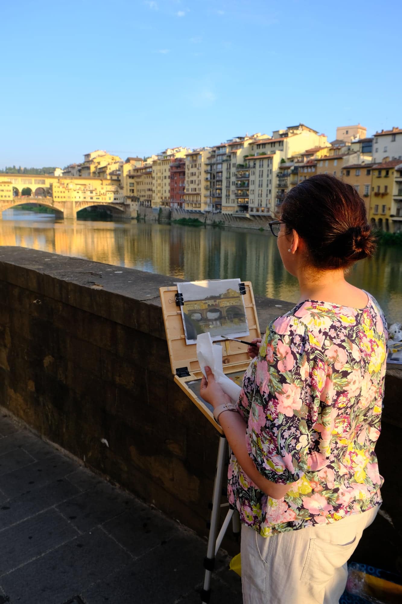 Tiana Goosen painting en plein air on the bank of the Arno in Florence, with the Ponte Vecchio behind her